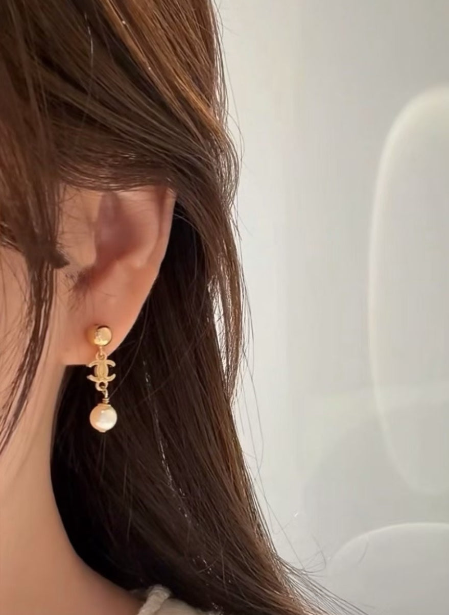 DreamStudio CHANEL gold-tone drop earrings with iconic CC logo and cream pearl accent worn on a woman's ear